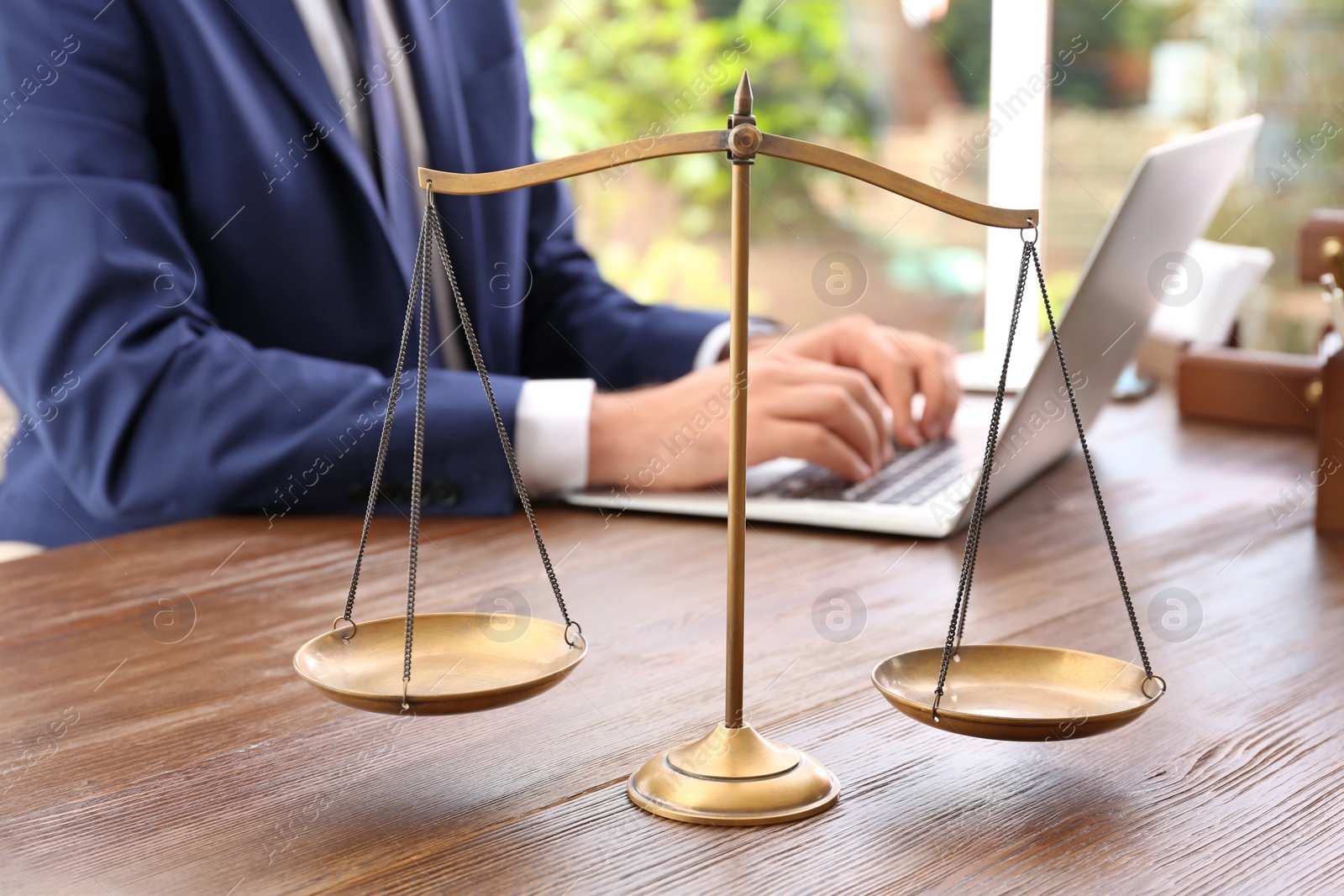 Photo of Scales of justice and blurred lawyer working with laptop on background