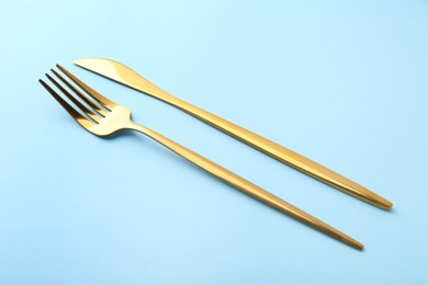 Photo of Stylish cutlery. Golden knife and fork on light blue background