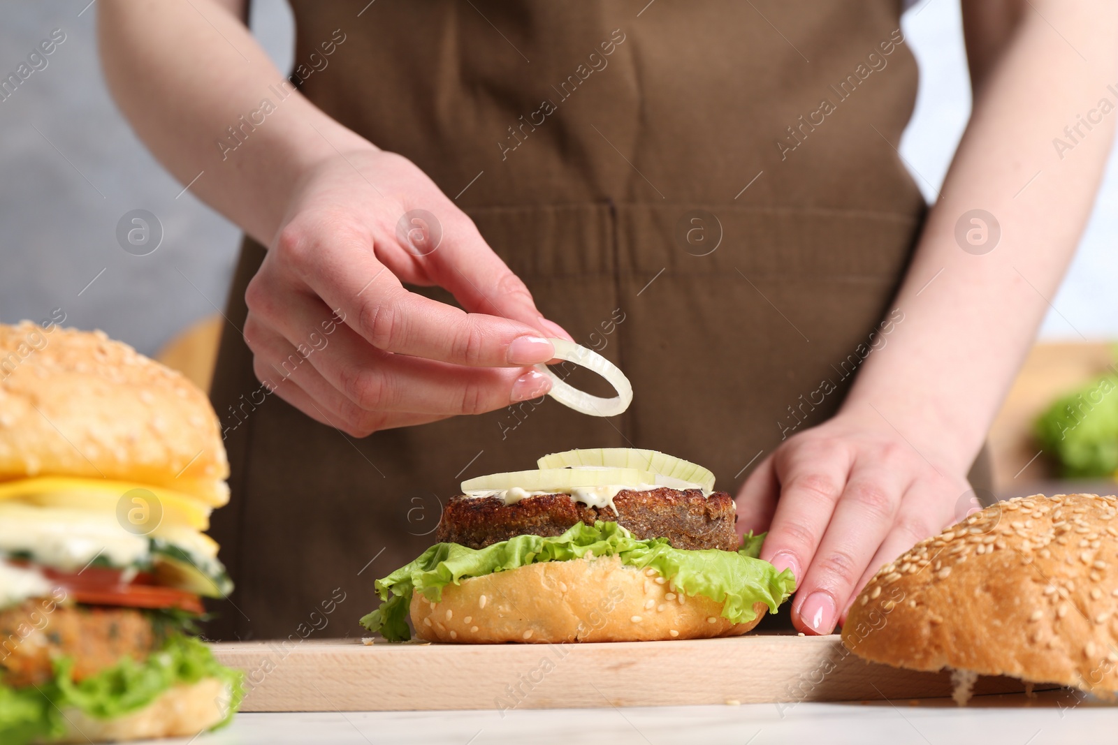 Photo of Woman making delicious vegetarian burger at table, closeup