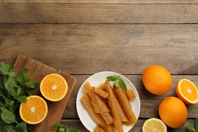 Photo of Delicious fruit leather rolls and oranges on wooden table, flat lay. Space for text