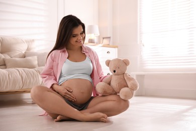 Photo of Young pregnant woman with toy bear at home