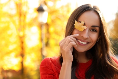Photo of Beautiful woman with yellow leaf in sunny park. Autumn walk