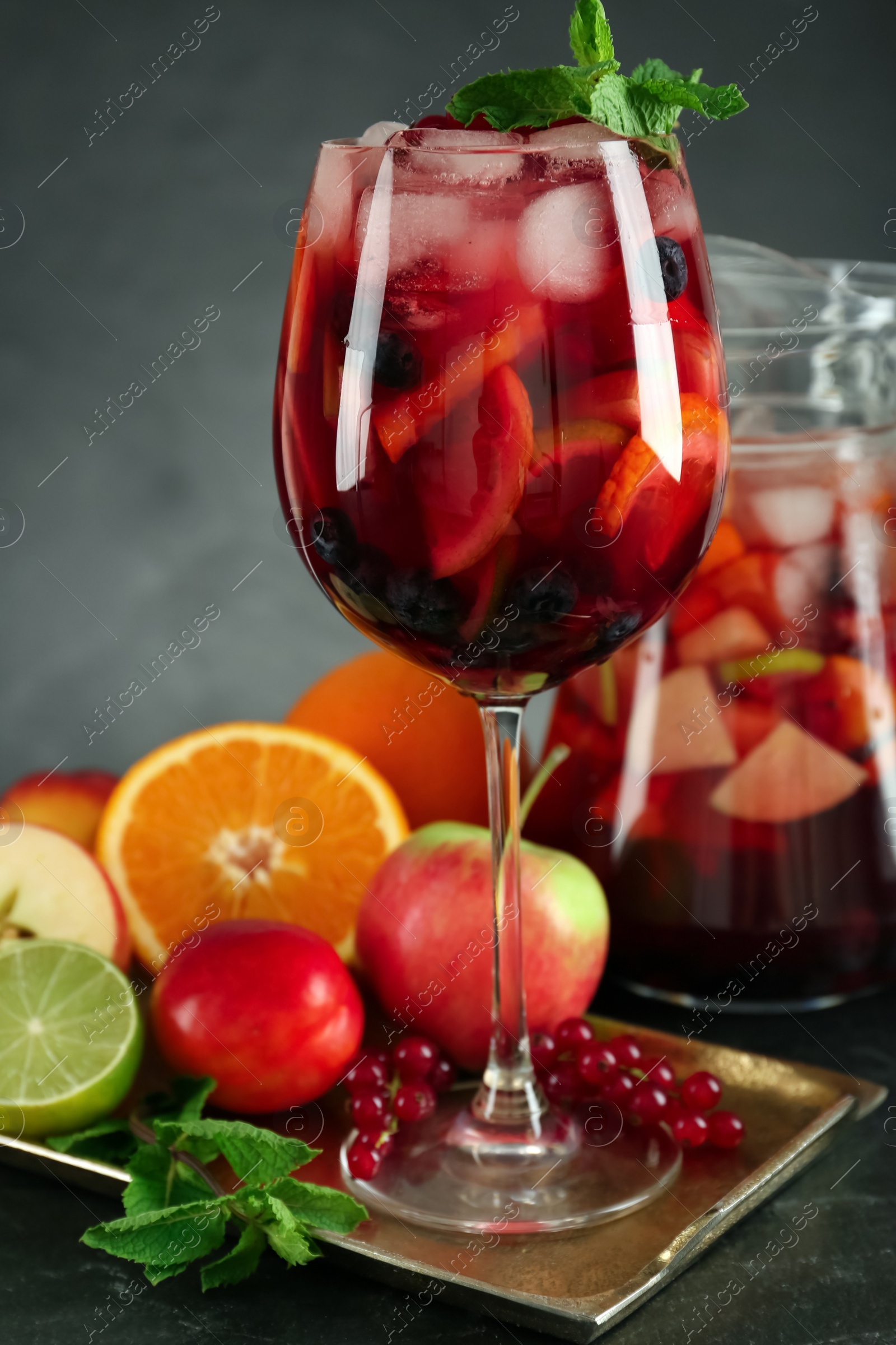 Photo of Glass and jug of Red Sangria with fruits on black table