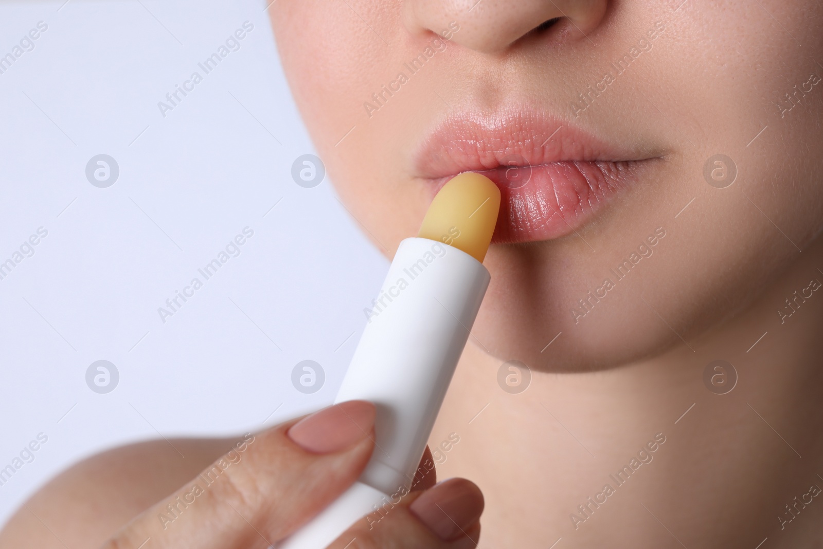 Photo of Woman applying hygienic lipstick on lips against white background, closeup