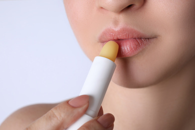 Photo of Woman applying hygienic lipstick on lips against white background, closeup