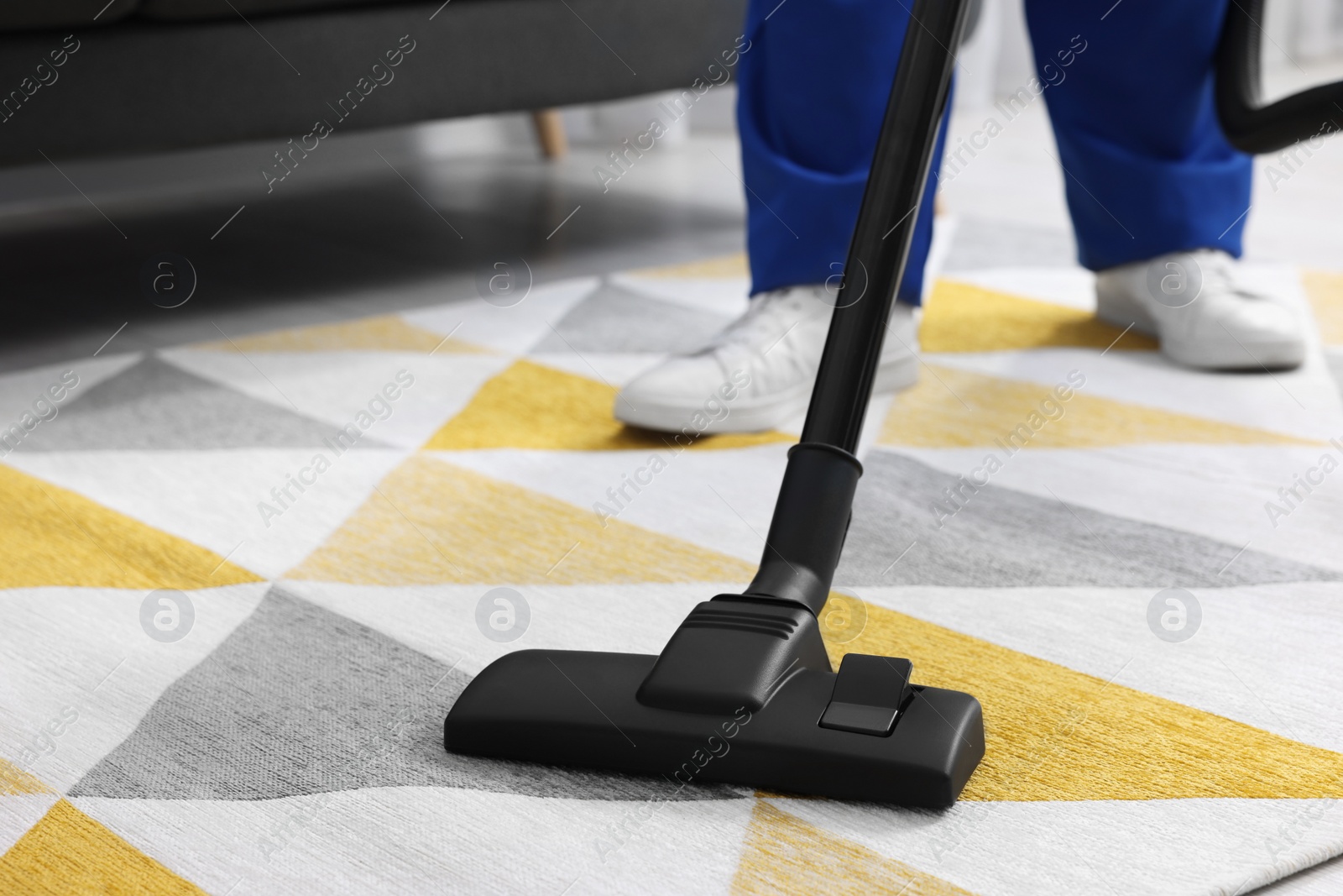 Photo of Dry cleaner's employee hoovering carpet with vacuum cleaner indoors, closeup