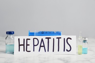 Word Hepatitis, vials and syringe on white marble table