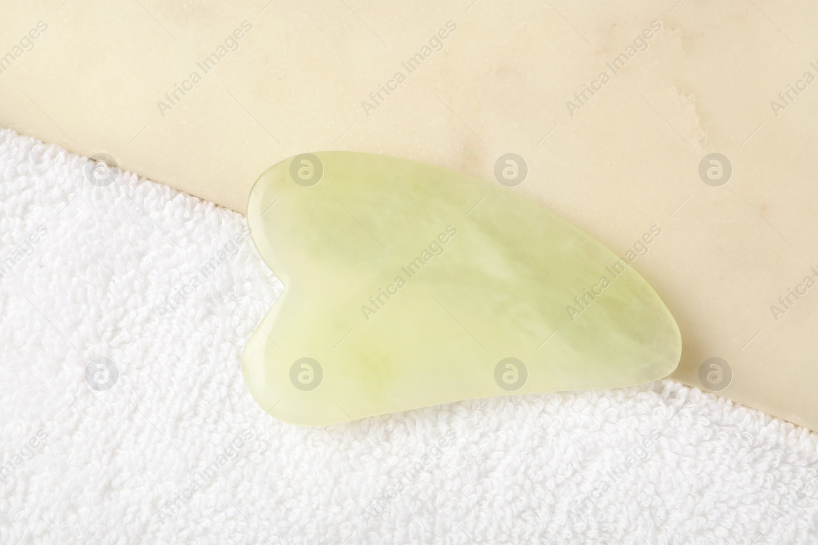 Photo of Jade gua sha tool and board on white towel, closeup