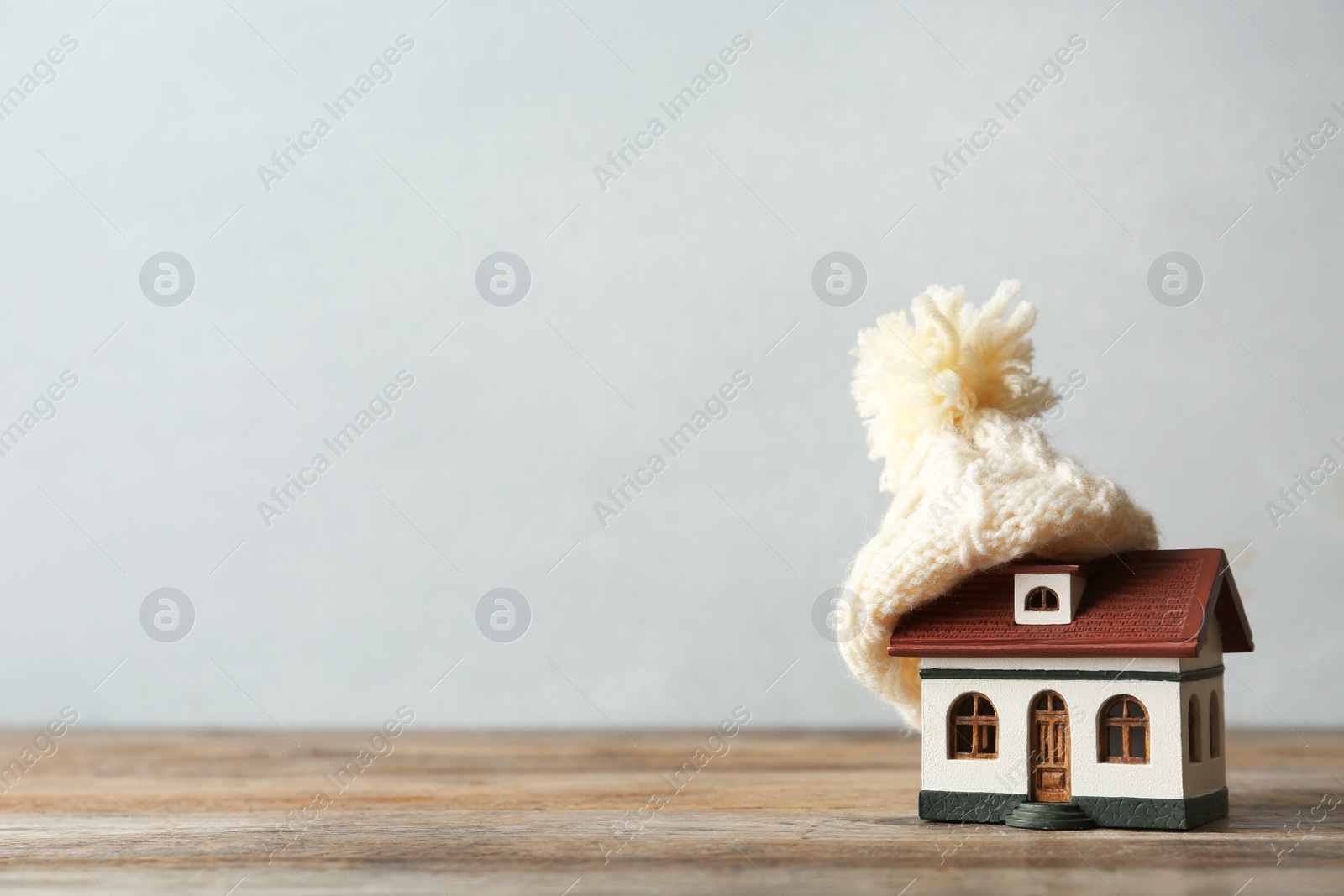 Photo of Wooden house model and hat on wooden table against light background, space for text. Heating efficiency