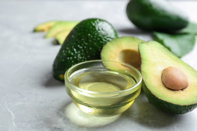 Photo of Bowl of natural oil and avocados on grey stone background