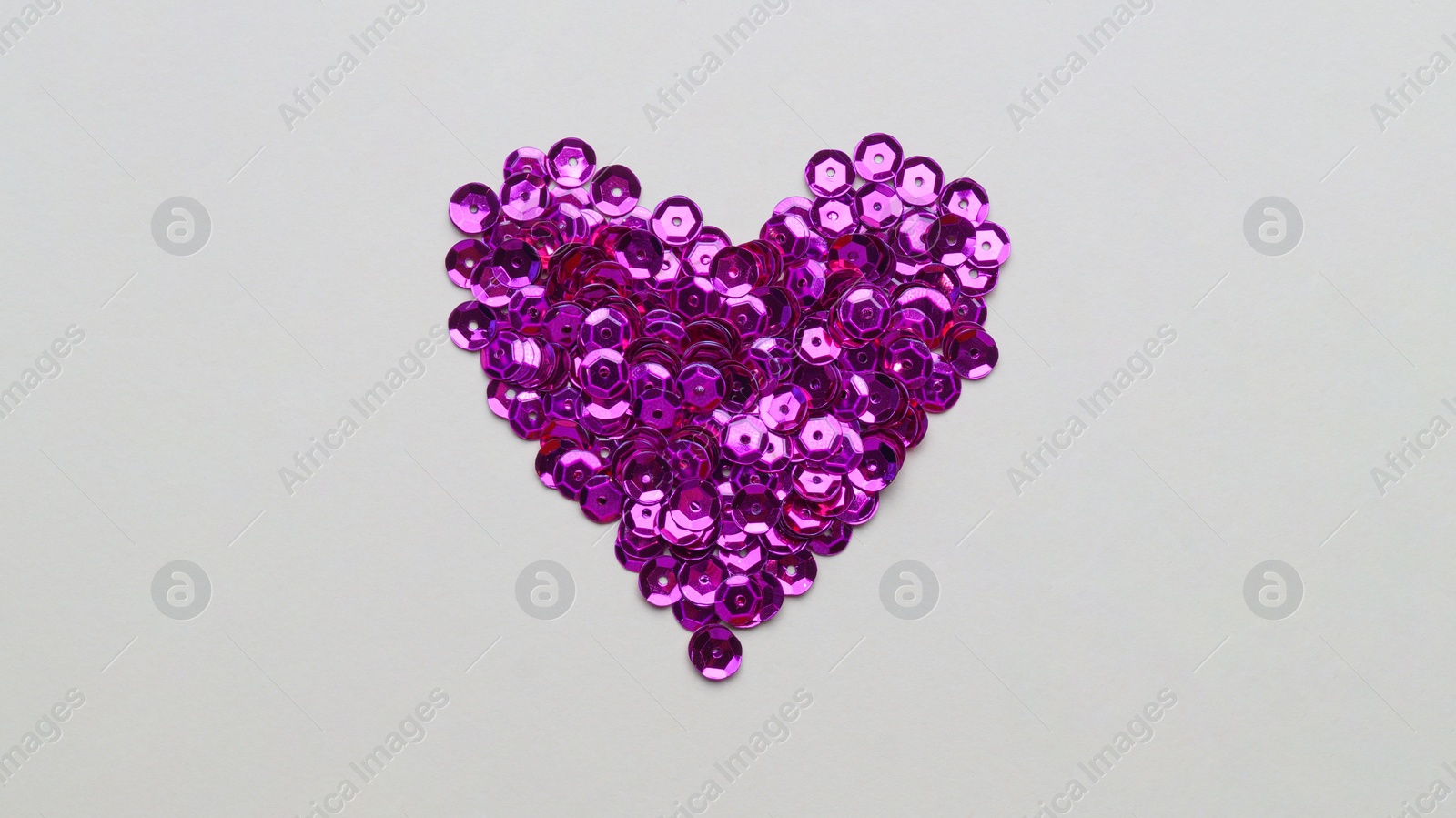 Photo of Purple sequins in shape of heart on light grey background, flat lay