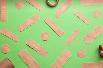 Different types of sticking plasters on green background, flat lay