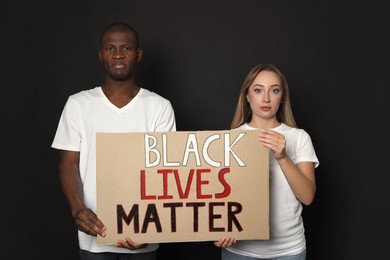 Photo of Young woman and African American man holding sign with phrase Black Lives Matter on dark background. Racism concept