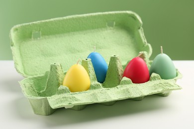 Photo of Colorful egg shaped candles in carton on white table. Easter decor