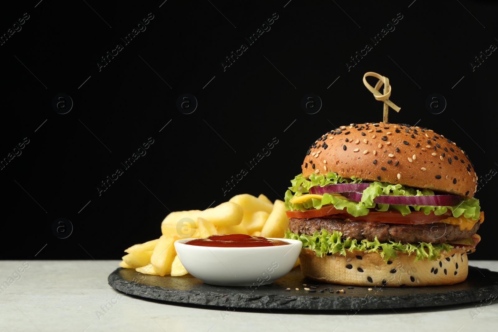Burger with delicious patty, french fries and sauce on gray table against black background, space for text Photo of Burger with delicious patty, french fries and sauce on gray table against black background, space for text