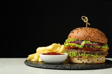 Photo of Burger with delicious patty, french fries and sauce on gray table against black background, space for text