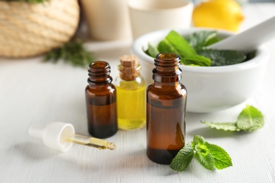 Bottles with mint essential oil on white wooden table