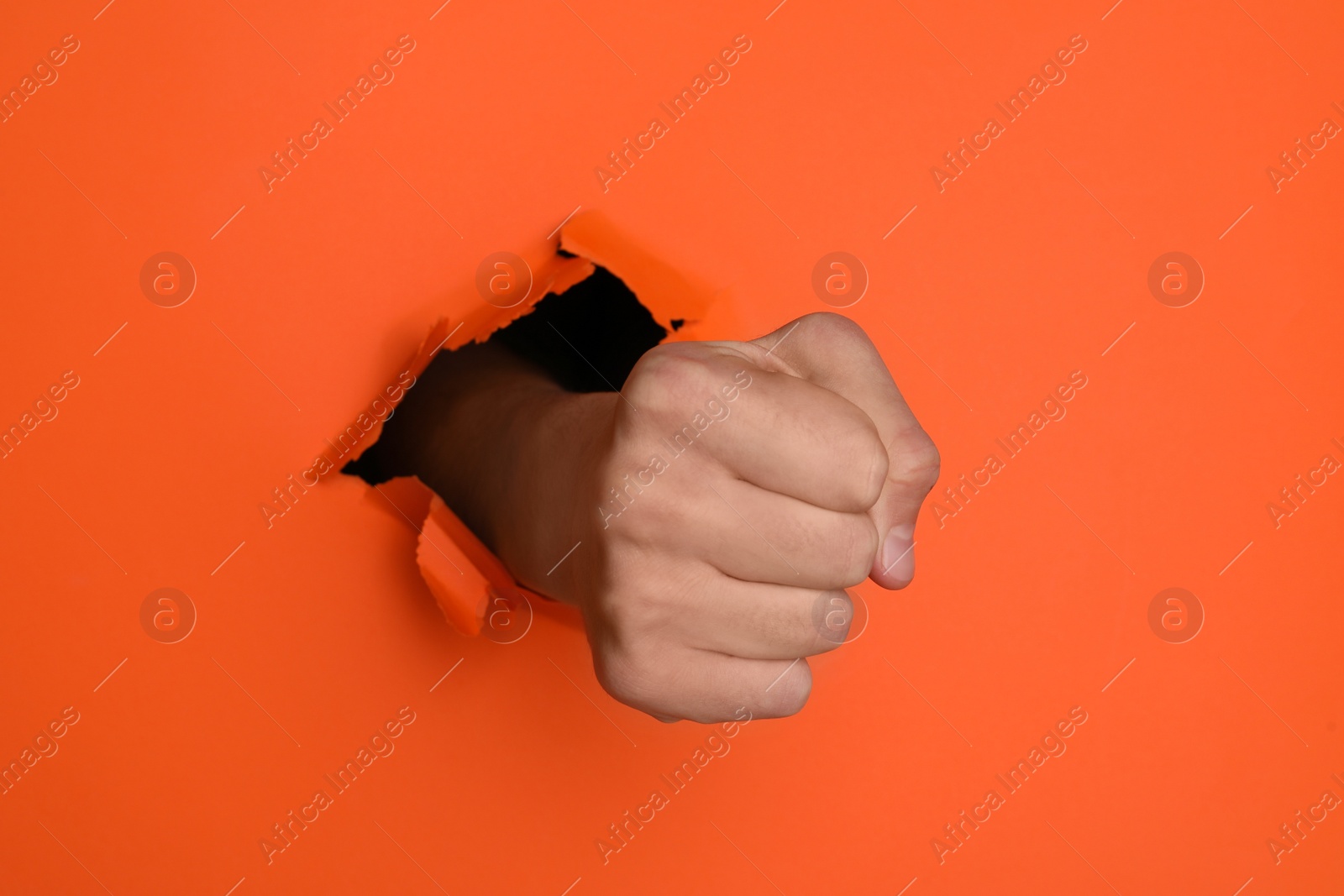 Photo of Man breaking through orange paper with fist, closeup