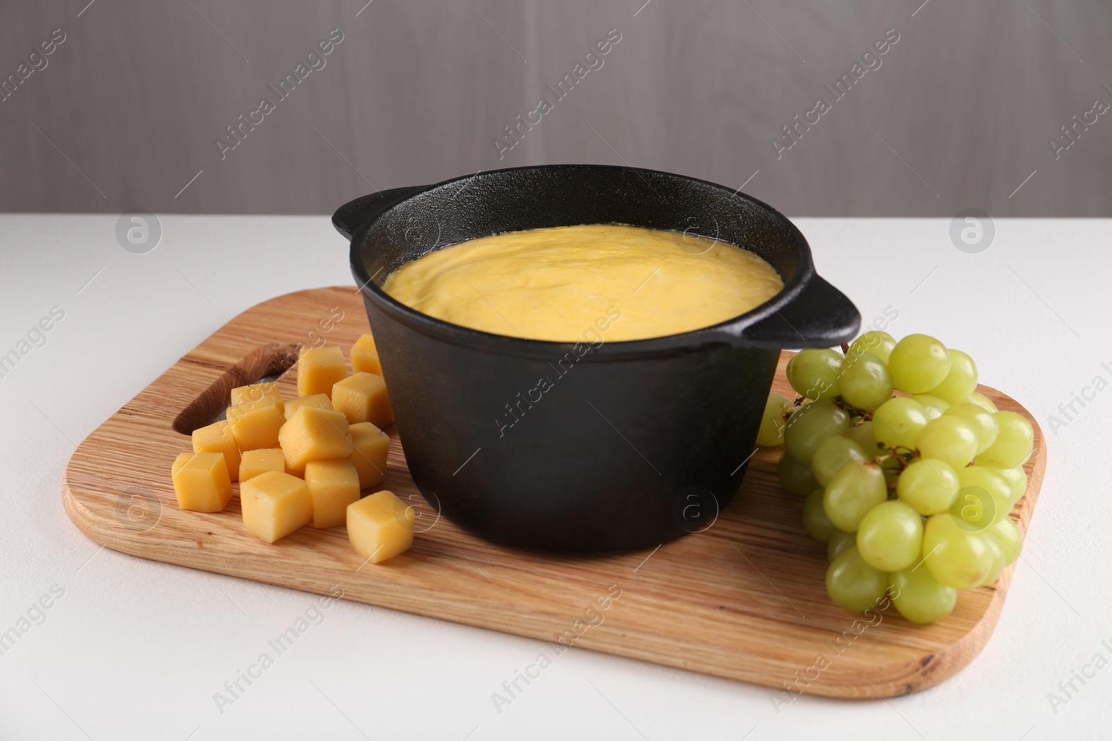 Photo of Fondue with tasty melted cheese and grapes on white table