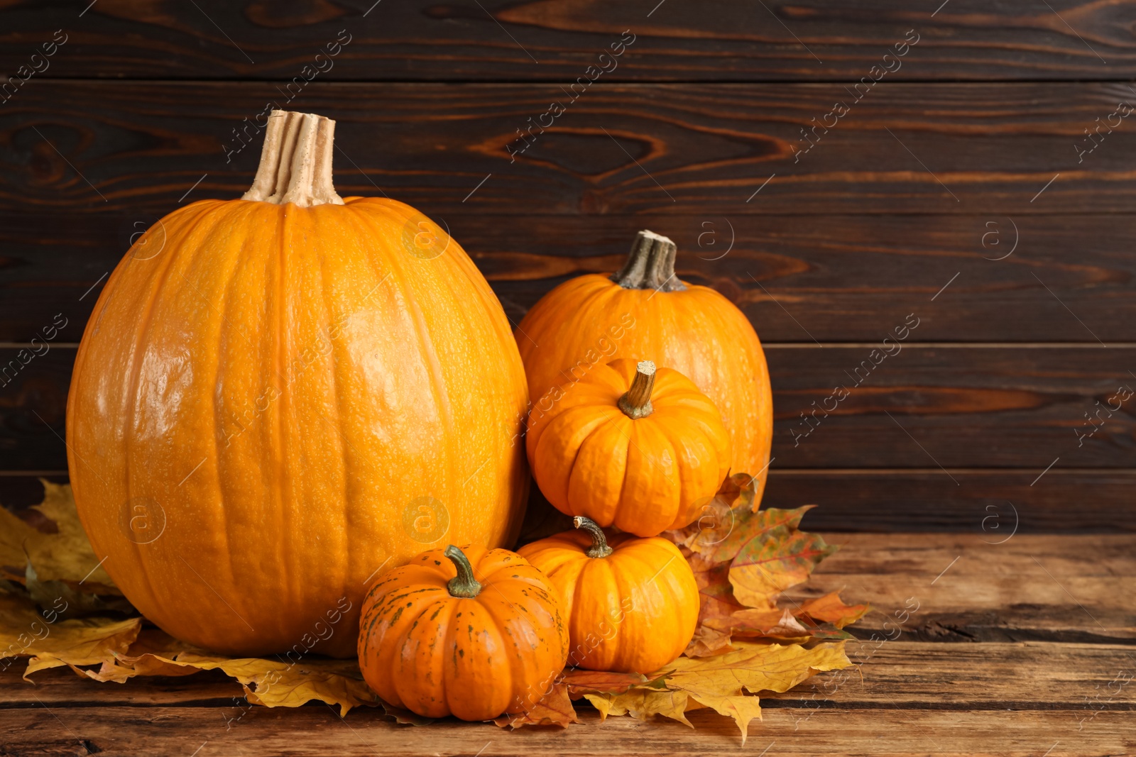 Photo of Pile of ripe pumpkins and dry leaves on wooden table, space for text