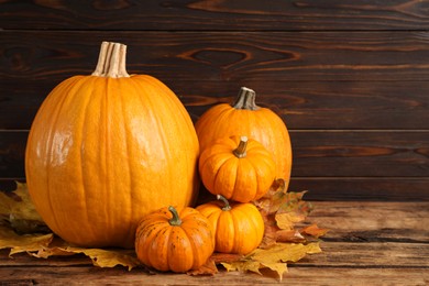 Photo of Pile of ripe pumpkins and dry leaves on wooden table, space for text