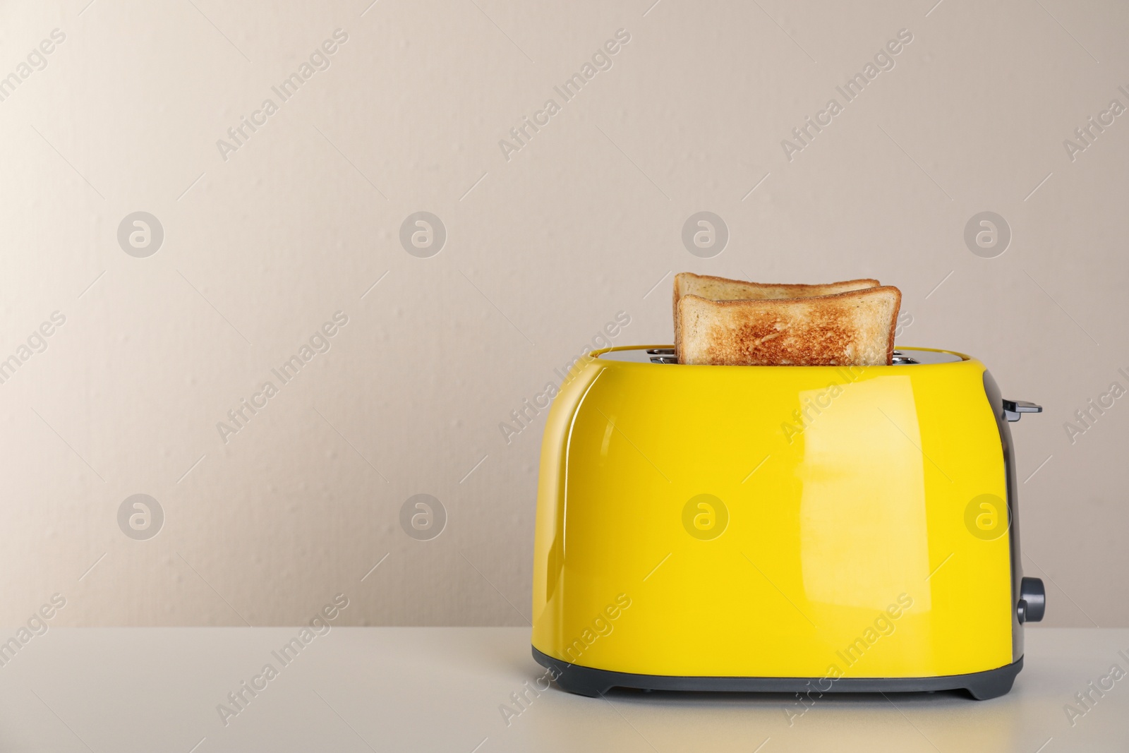 Photo of Electric toaster with bread slices on light table. Space for text