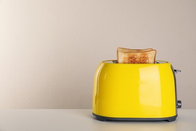 Photo of Electric toaster with bread slices on light table. Space for text