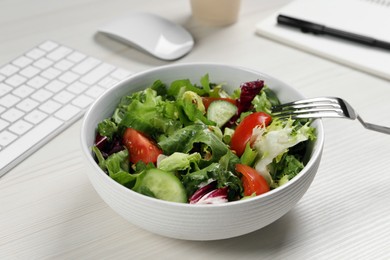 Bowl of tasty food, fork and keyboard on white wooden table, closeup. Business lunch