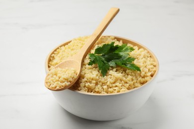 Delicious bulgur with parsley and spoon on white marble table, closeup