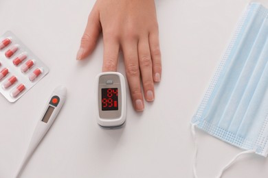 Photo of Woman measuring oxygen level with modern fingertip pulse oximeter at white table, top view