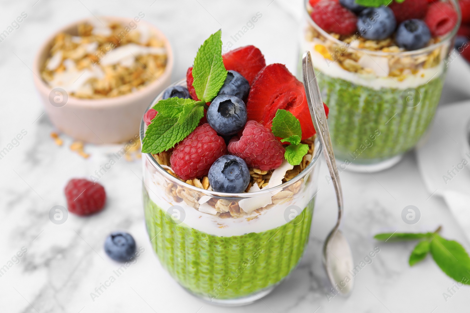 Photo of Tasty matcha chia pudding with oatmeal and berries on white marble table, closeup. Healthy breakfast