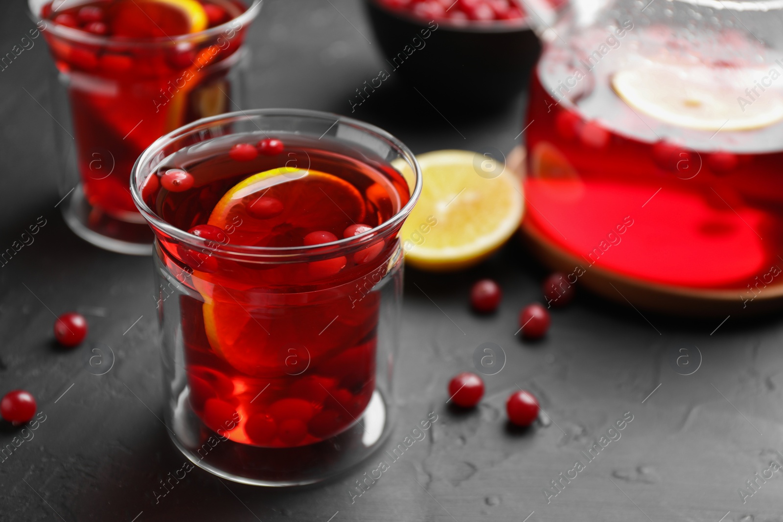 Photo of Tasty hot cranberry tea with lemon and fresh berries in glass on black textured table