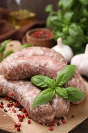 Photo of Raw homemade sausages and different spices on wooden board, closeup