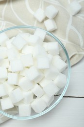 Photo of Many sugar cubes in glass bowl on white wooden table, top view