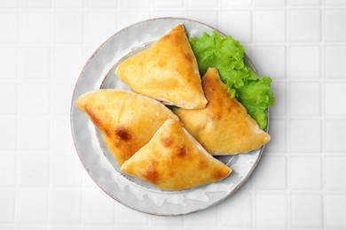 Delicious samosas and lettuce on white tiled table, top view