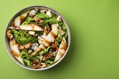 Photo of Delicious pear salad with sauce in bowl on green background, top view. Space for text