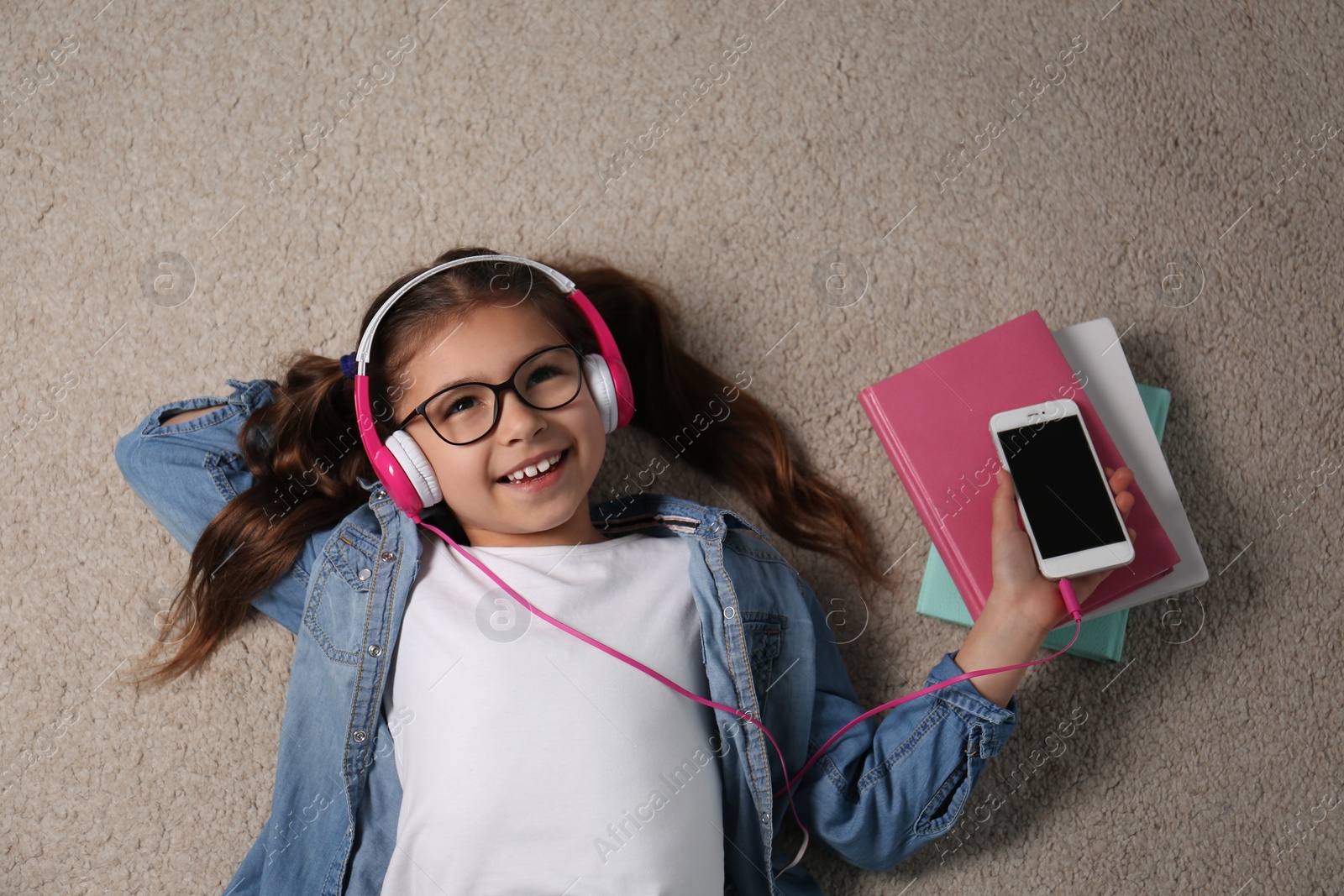 Photo of Cute little girl listening to audiobook on floor, top view