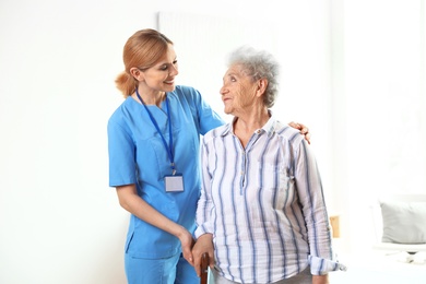 Nurse in uniform assisting elderly woman indoors