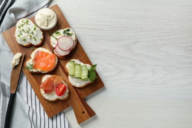 Toasted bread with cream cheese and different toppings on white wooden table, flat lay. Space for text