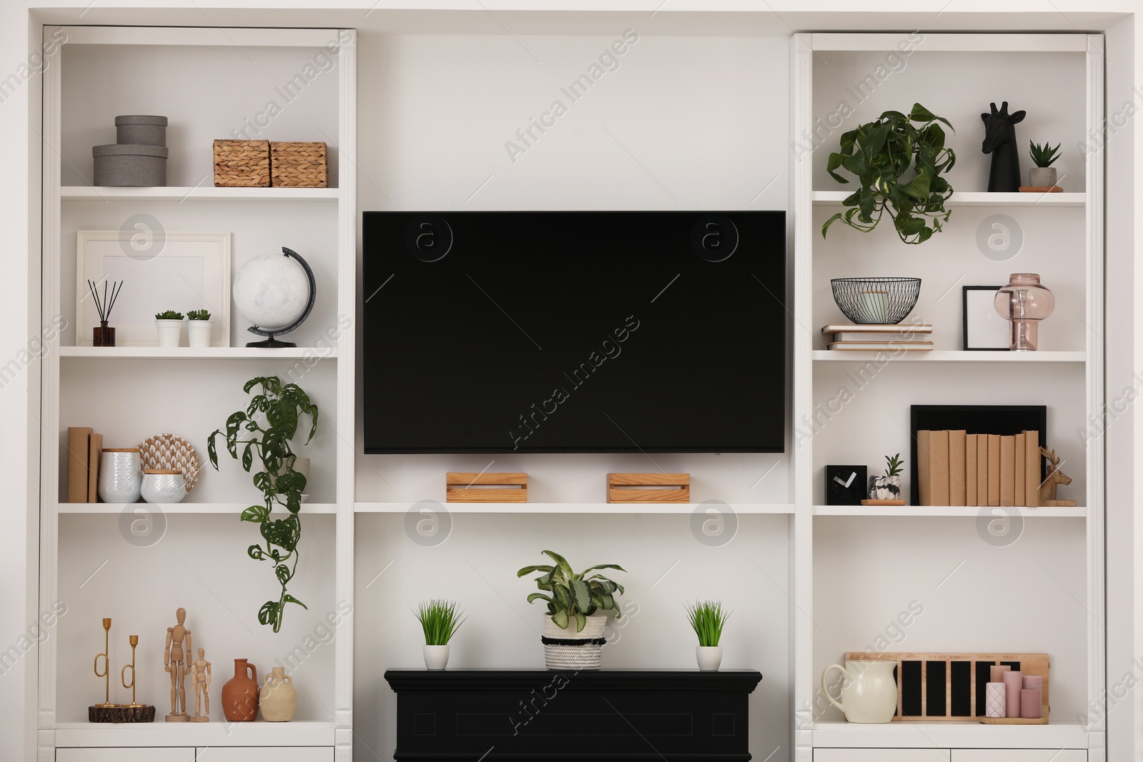 Photo of Modern TV set and shelves with decor near white wall. Interior design