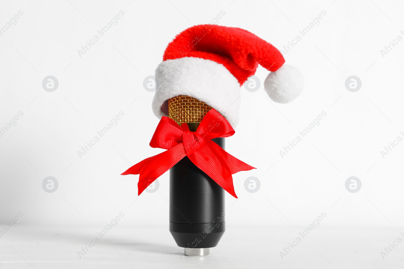 Photo of Microphone with Santa hat and red bow on white background. Christmas music