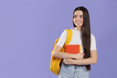 Photo of Happy teenage girl with backpack and textbooks on violet background. Space for text