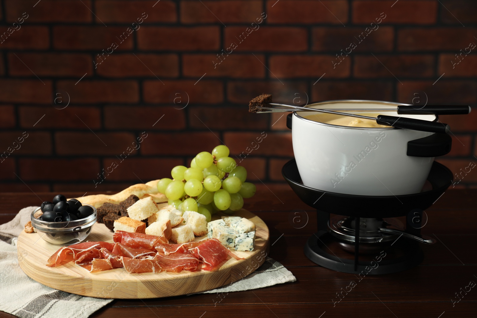 Photo of Fondue with tasty melted cheese, forks and different snacks on wooden table