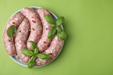 Photo of Raw homemade sausages, basil leaves and peppercorns on green table, top view. Space for text