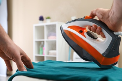 Man ironing clothes on board at home, closeup