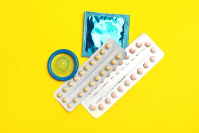 Photo of Condoms and birth control pills on yellow background, flat lay. Safe sex concept