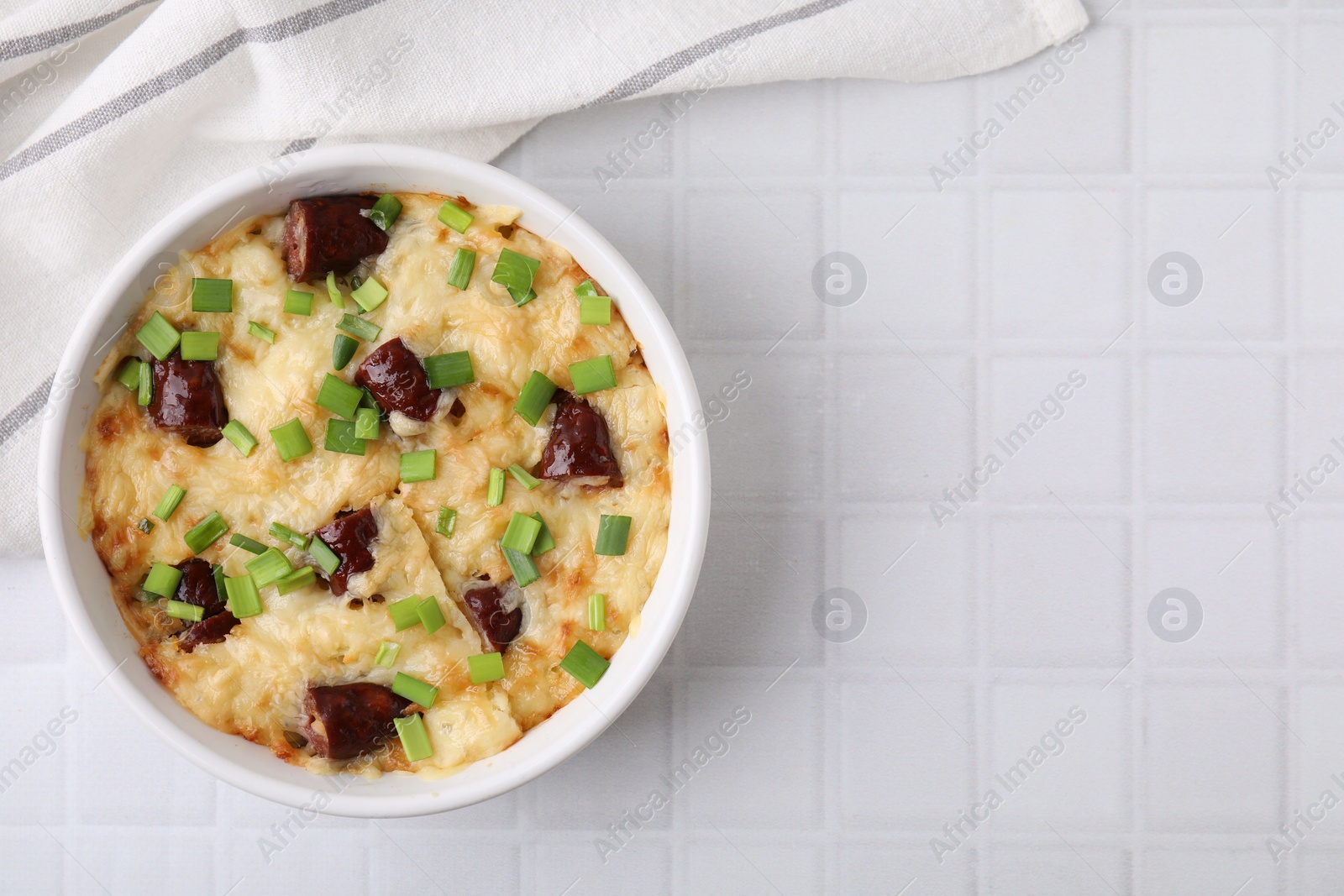 Photo of Tasty sausage casserole in baking dish on white tiled table, top view. Space for text