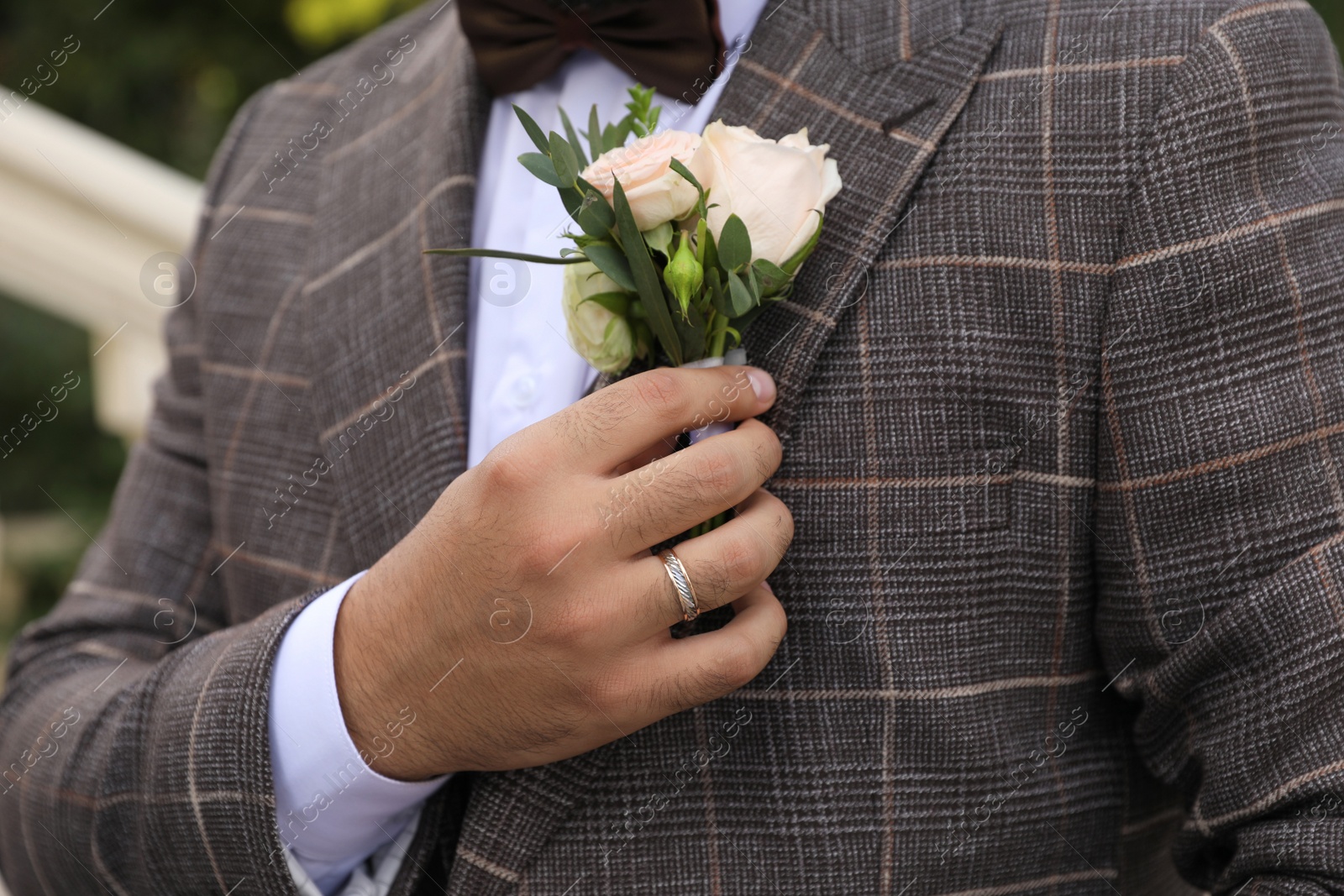 Photo of Groom wearing engagement ring with beautiful boutonniere outdoors, closeup. Preparing for wedding