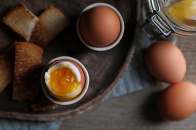 Photo of Tasty boiled eggs in cups on wooden table, flat lay