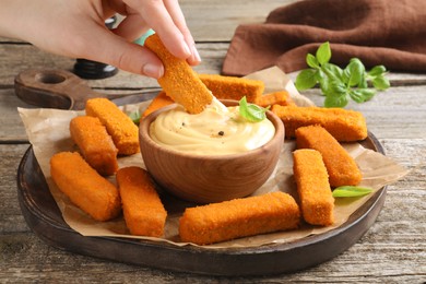 Photo of Woman dipping delicious chicken nuggets into cheese sauce at wooden table, closeup